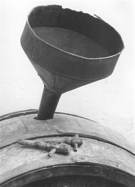 Imbuto di latta a cono rovesciato inserito in una botte con accanto alcune cannelle per spillare il vino
