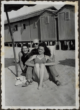 Ritratto di due ragazze e un uomo seduti sulla spiaggia di uno stabilimento balneare